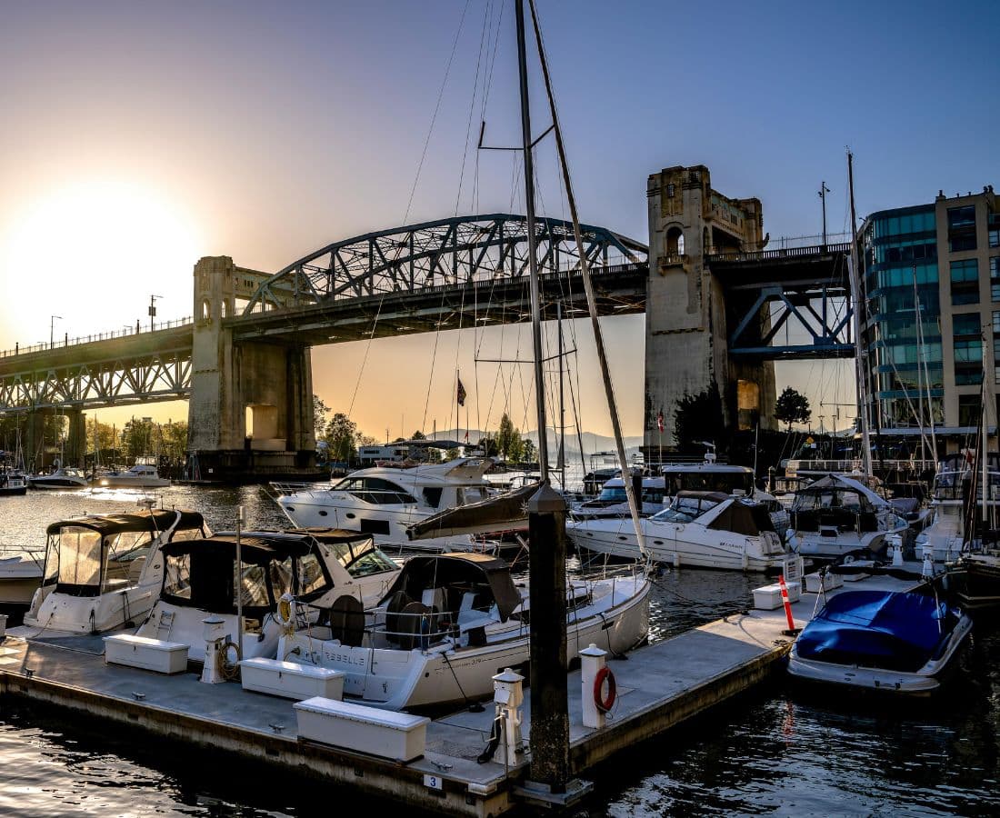 Crystal Gloss technician polishing a boat hull at a Vancouver marina — False Creek with Burrard Bridge at sunset